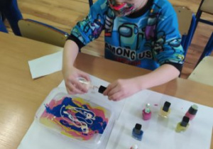 Uczeń wylewa farbę na wodę .Stworzył wielobarwną kompozycję.